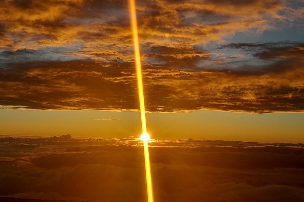 spectacular sunset in La Réunion, with a vertical shaft of light and a golden sky above the clouds