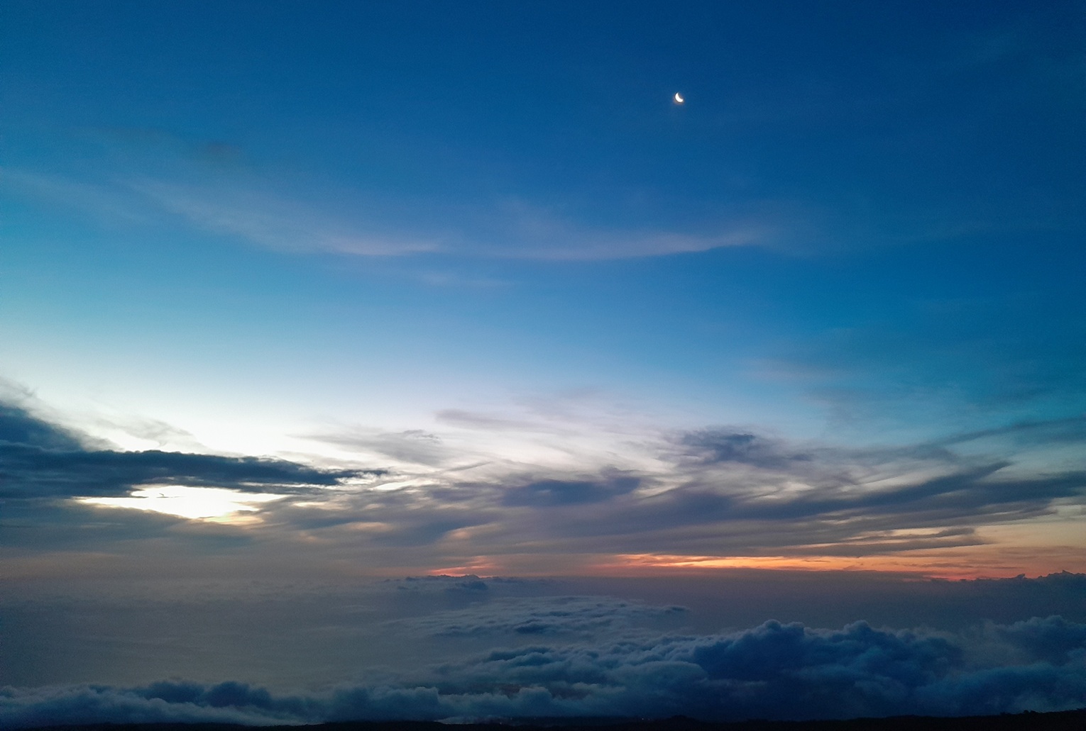 sunset in La Réunion, with a deep blue sky and a crescent moon above a sea of clouds