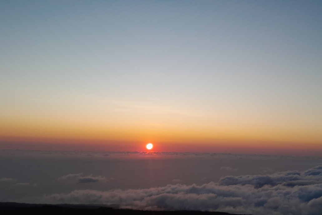 sunset in La Réunion, with the sun piercing the clouds and coloured mist above the ocean
