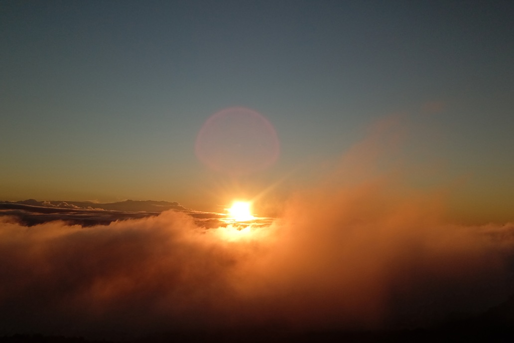luminous sunset in La Réunion, with the sun piercing the clouds and golden mist above the relief