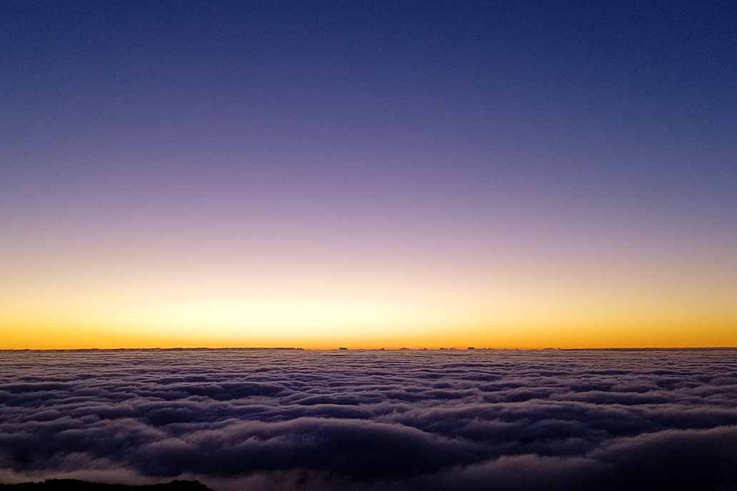 minimalist sunset in La Réunion, with an orange horizon and a dark sea of clouds beneath a clear sky